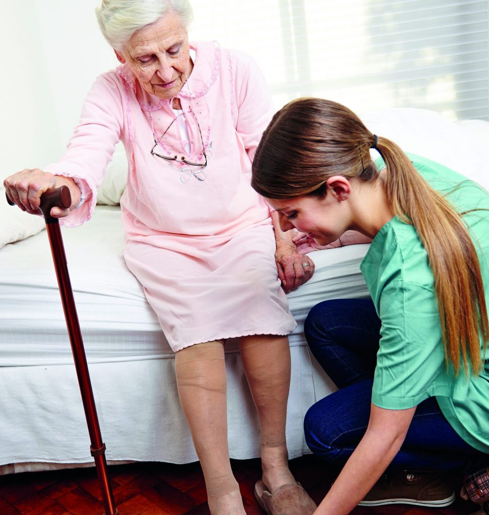 Kvinna hjälper en gammal kvinna på med sina tofflor